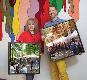 Eileen and Alex Kunzman with framed paintings in front of a stylized mural of paint dripping
