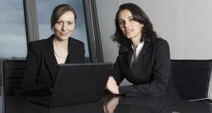 two female lawyers, one with a laptop, looking at the camera